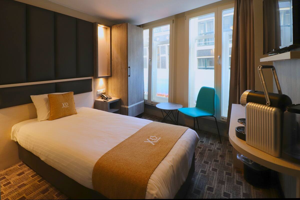 Een hotelkamer met een groot bed, een bureau met telefoon, een stoel, een klein tafeltje en een radiator.