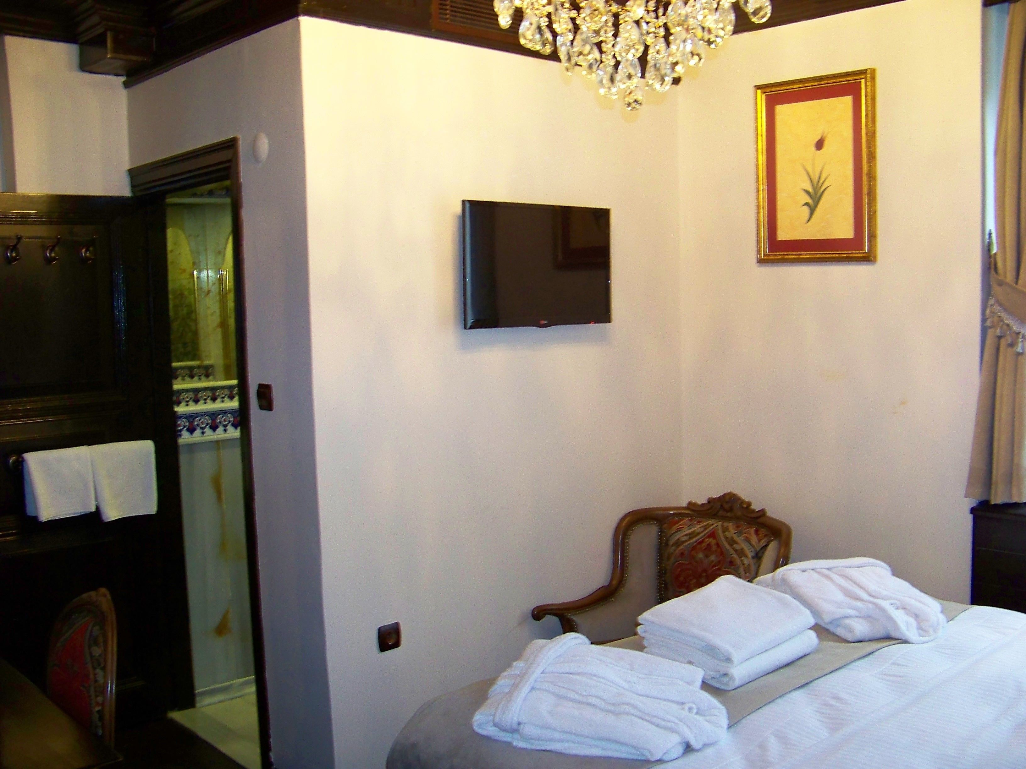 A hotel room with a bed, a television mounted on the wall, a chandelier, and a framed picture.