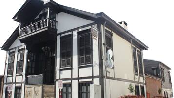 Um edifício de dois andares com varanda, janelas amplas com persianas e uma placa indicando que é um hotel.