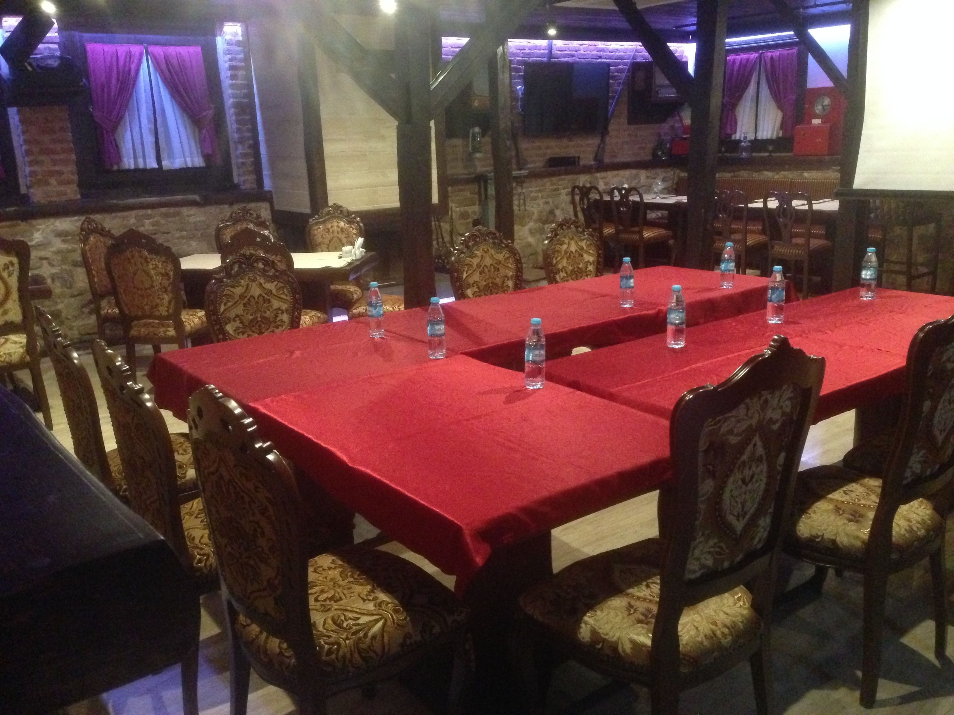 Un restaurant avec des nappes rouges, des chaises en bois et des bouteilles d’eau sur les tables.