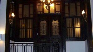 A wooden staircase with a black balustrade leading to a dark wooden door with a glass panel and a decorative iron gate. - Hotel Edirne Osmanli Evleri (Edirne)