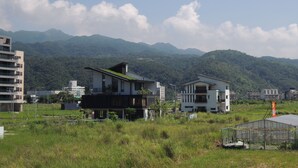 Un edificio moderno con techo plano y una sección de techo ajardinada, rodeado de un campo cubierto de hierba y montañas al fondo.
