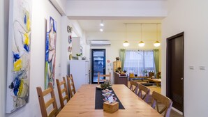 Un comedor con una mesa de madera, sillas y un mantel individual negro. Hay pinturas abstractas en la pared y una zona de cocina al fondo.