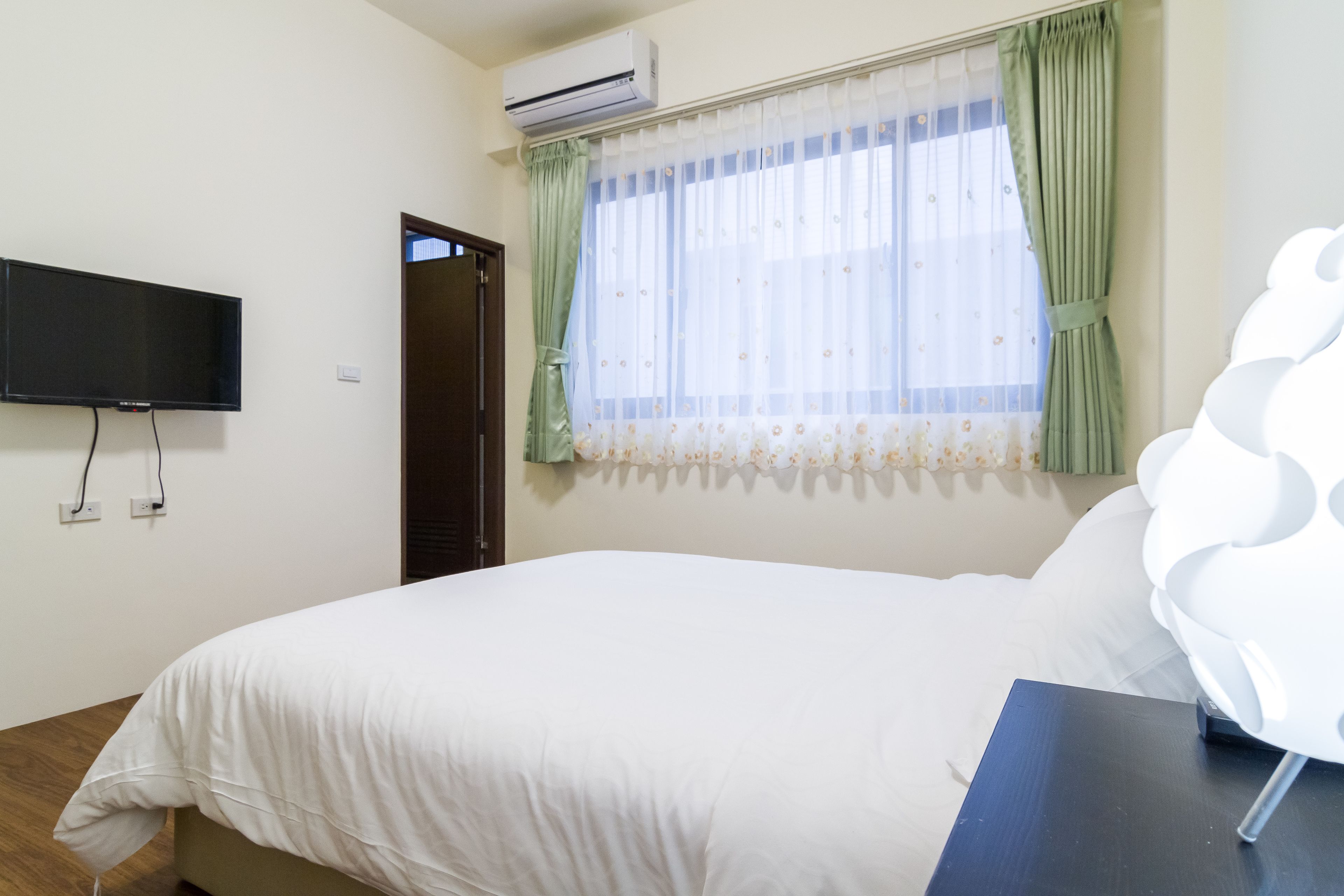 Une chambre à coucher avec un lit, un téléviseur fixé au mur et une fenêtre avec des rideaux.