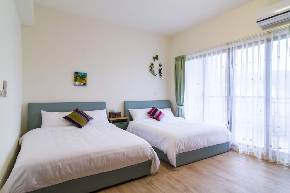 Une chambre d’hôtel avec deux lits, une petite table et une fenêtre avec des rideaux légers.
