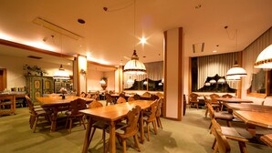 A dining area with multiple wooden tables and chairs, overhead lighting, and a green carpet. - Marillen Hotel (Hakuba)