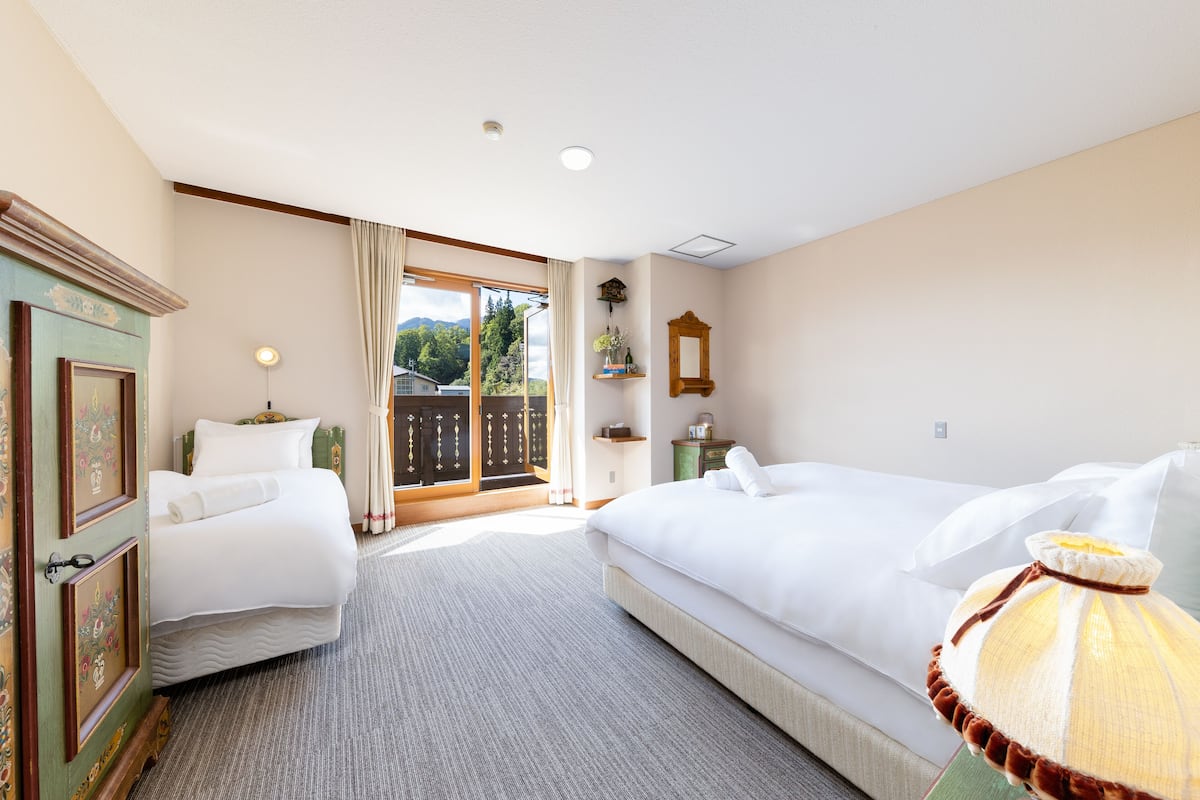 Habitación de hotel con dos camas, un ventanal con vistas, un armario de madera y una lámpara.