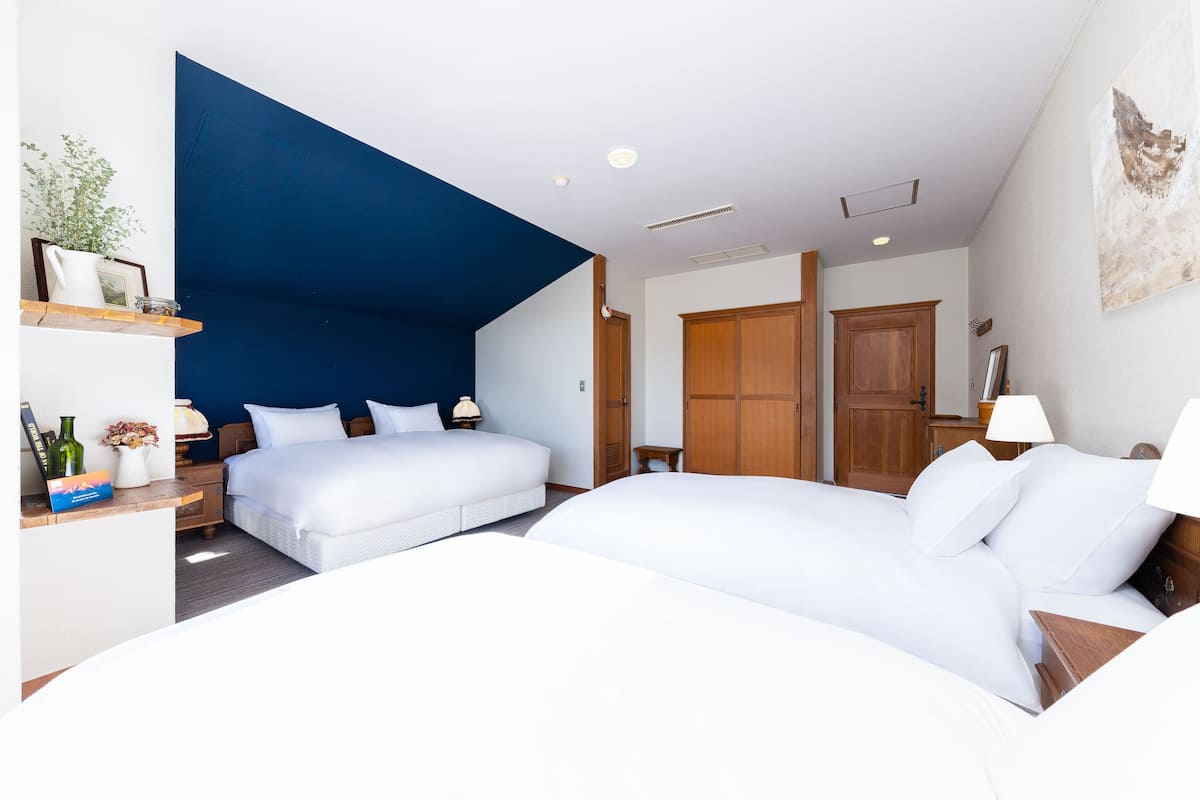 Una habitación de hotel con dos camas, una pared azul de acento, muebles de madera y un cuadro en la pared.