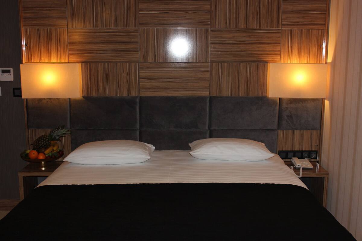 Une chambre d’hôtel avec un grand lit, deux lampes de chevet, un panier de fruits sur la table de chevet et un téléphone.