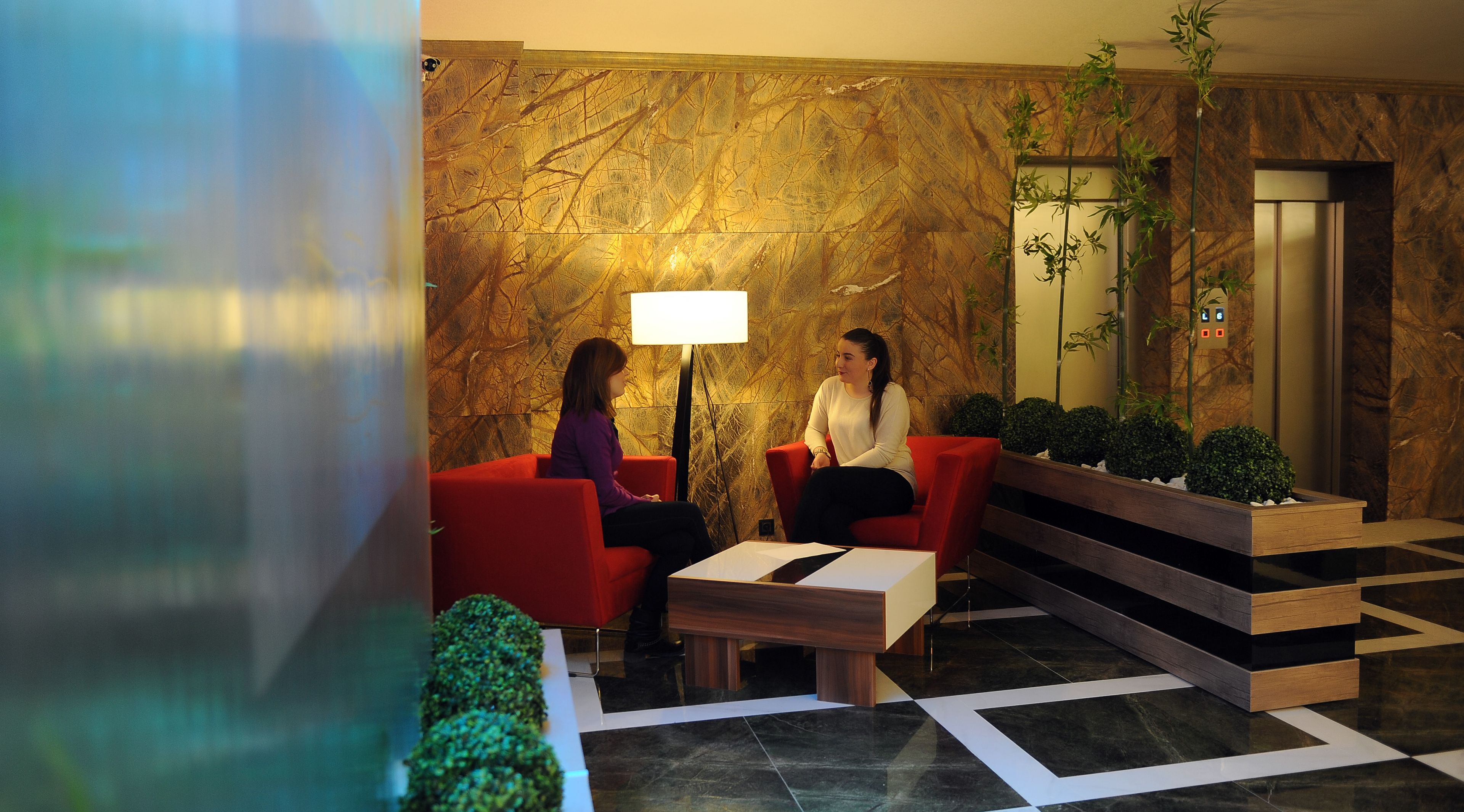 Eine Lobby mit roten Sitzgelegenheiten, einer Stehlampe, einem Spiegel und einer Treppe.