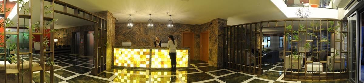 Een hotellobby met een zwart-witte vloer, een receptiebalie en een zithoek met planten.