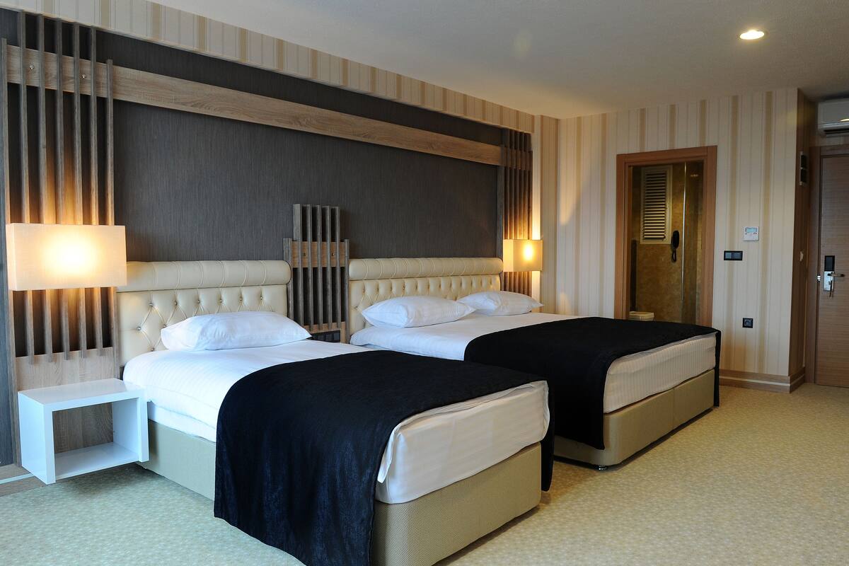 Une chambre d’hôtel avec deux lits, une table de chevet, une lampe fixée au mur et une porte avec une serrure.