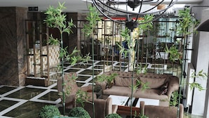 Um hall de entrada com um candelabro, cadeiras verdes, um sofá e um padrão quadriculado no chão.