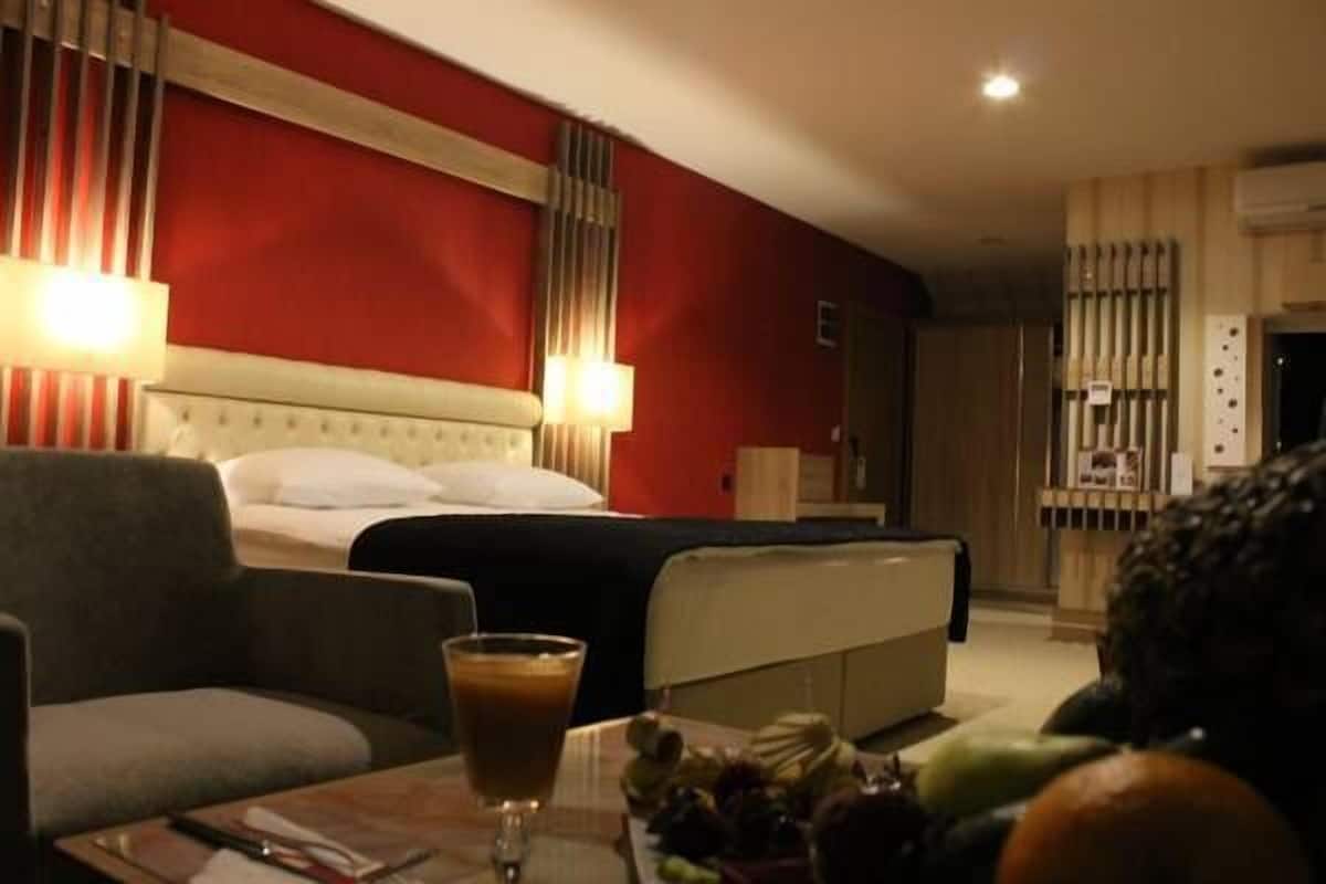 Une chambre d’hôtel avec un lit, un canapé, une table avec une boisson et des fruits, et une lampe.