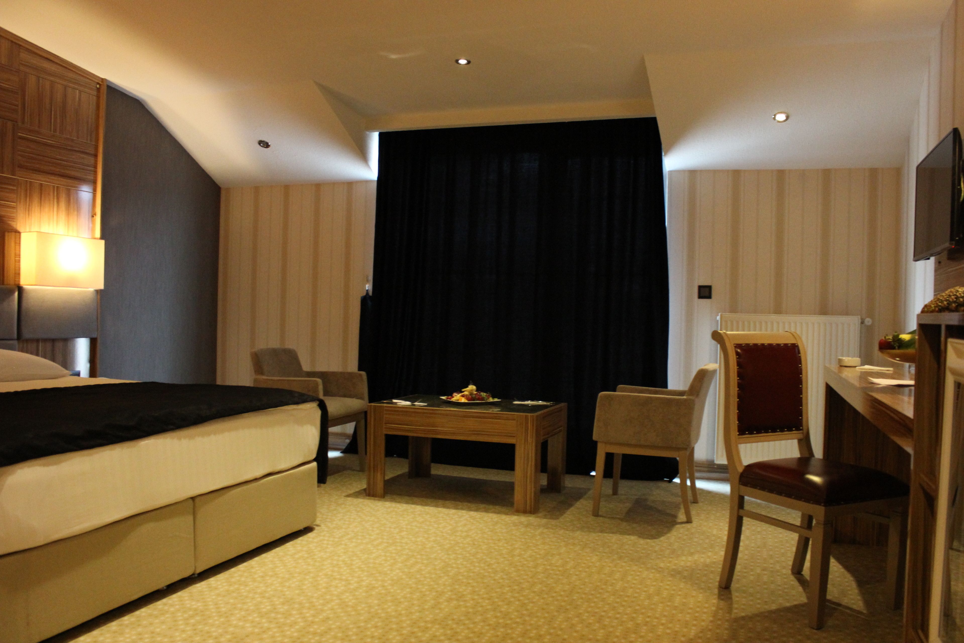 A hotel room with a bed, two chairs, a small table, a TV, and a window with curtains.
