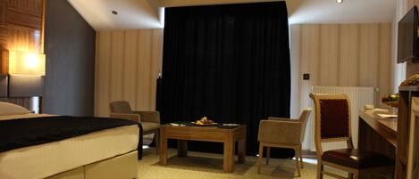 A hotel room with a bed, two chairs, a small table, a TV, and a window with curtains.