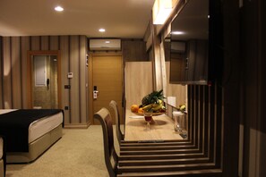 Una habitació d'hotel amb un llit, una taula de menjador amb fruita, una cadira i un televisor.