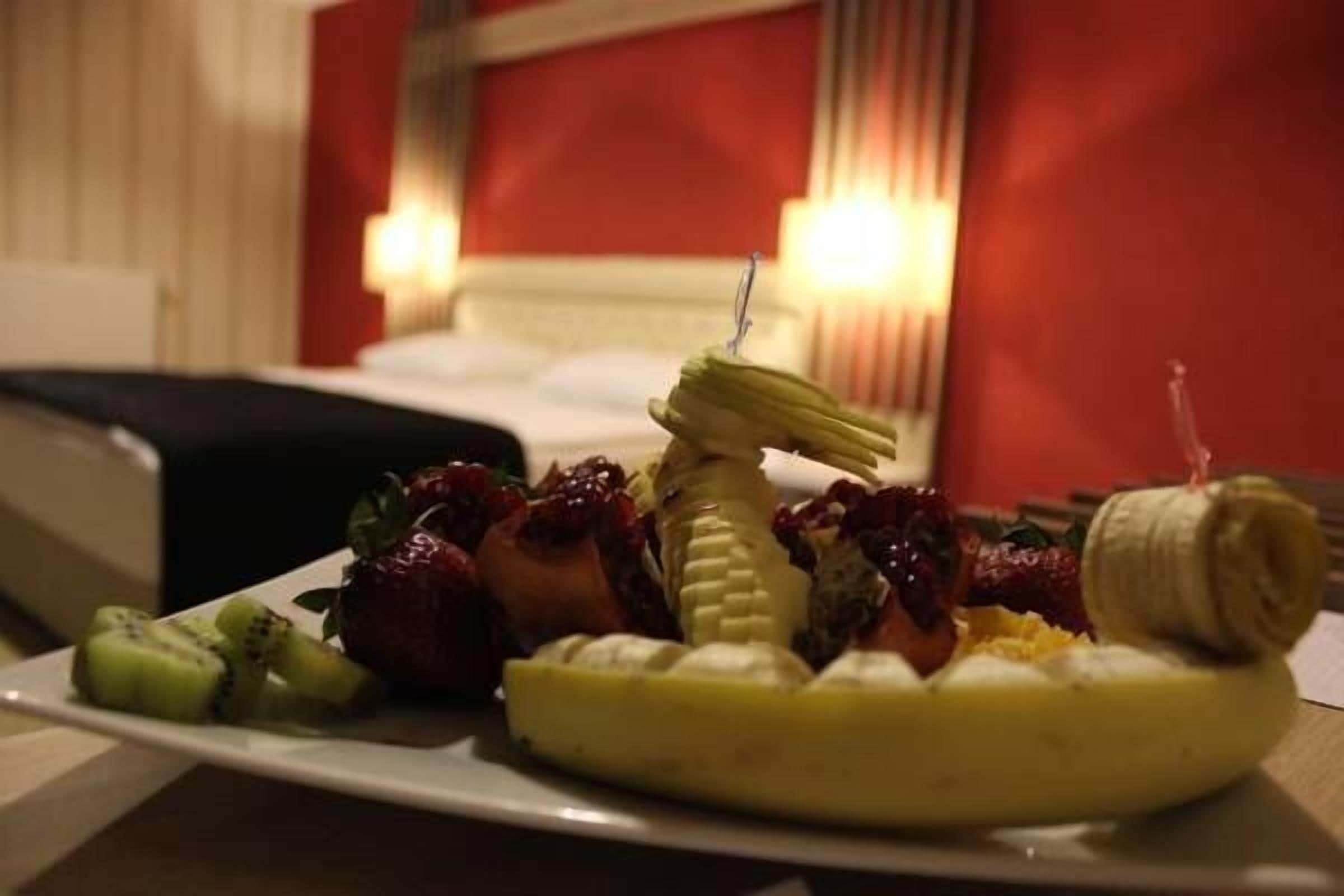 Un plato de fruta sobre una mesa, con una cama y una pared roja al fondo.