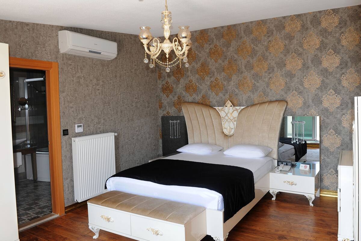 Une chambre à coucher avec un grand lit, une commode, une table de chevet, un climatiseur et un lustre.