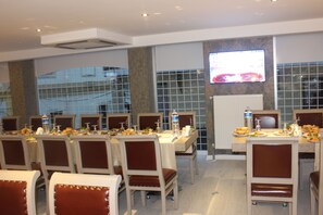 A dining area with multiple tables and chairs, a television screen, and a tiled wall. - Neba Royal Hotel (Samsun)