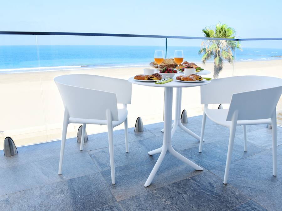 A balcony with a table set for two, overlooking a beach.