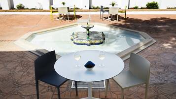 A round table with two chairs, a small fountain, and two glasses of wine.