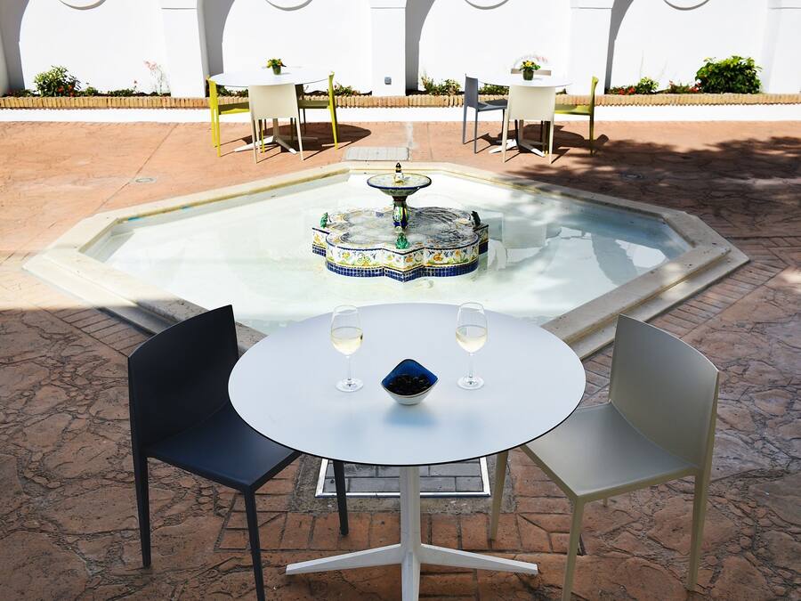 A round table with two chairs, a small fountain, and two glasses of wine.