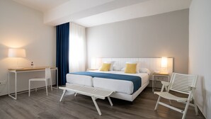 Una habitación de hotel moderna con una cama grande, un escritorio, dos sillas y una mesita de noche con lámpara.