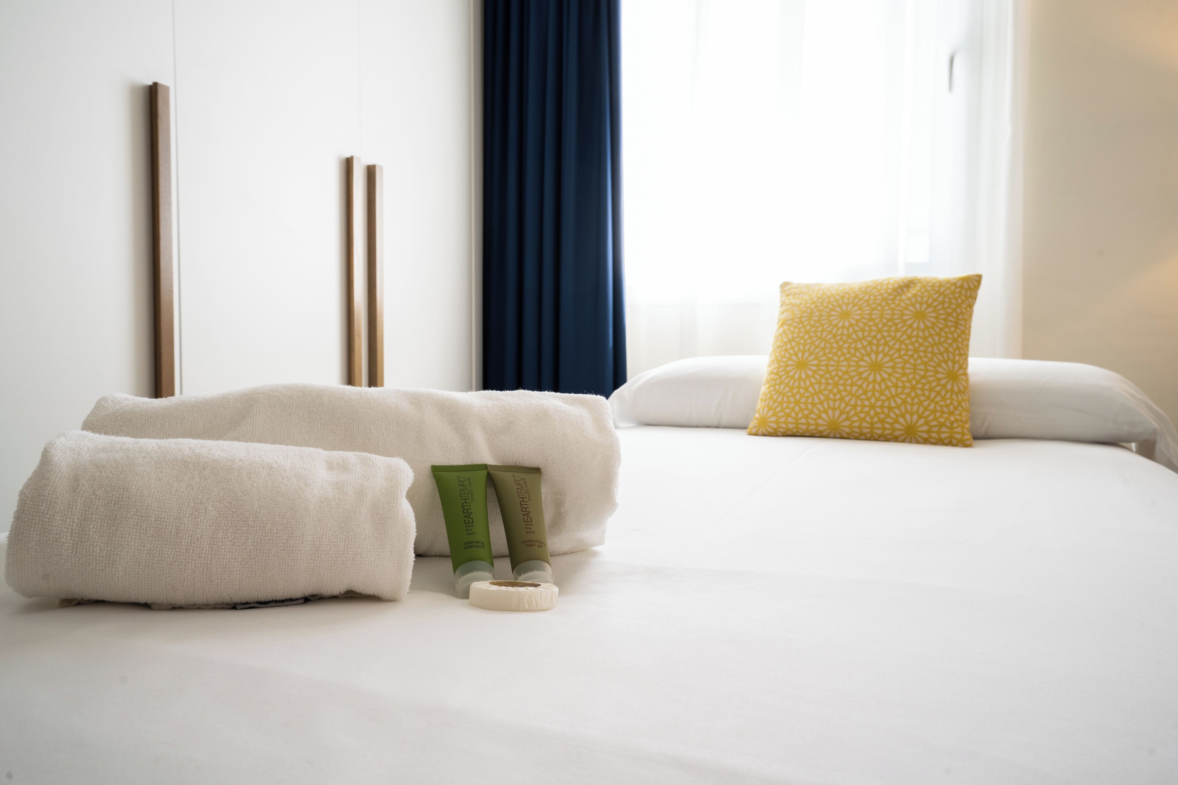 Una habitación de hotel con cama, toallas, almohada y ventana con cortinas.