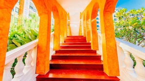 A staircase with red steps and white balustrades, surrounded by orange arches and greenery.