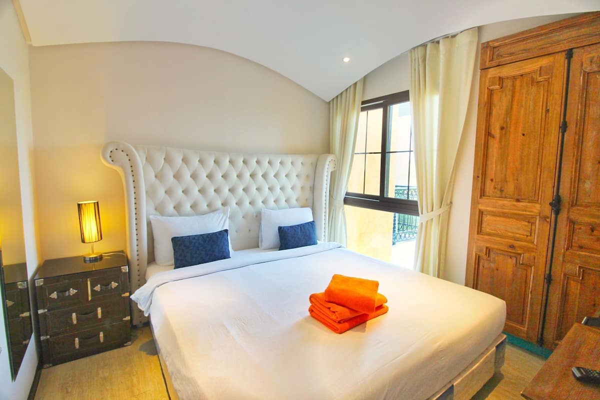 Una habitación de hotel con una cama grande, una mesita de noche, un aparador y un armario de madera.