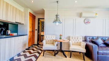 Una cocina moderna con armarios blancos, un suelo con estampado blanco y negro, una zona de comedor con dos sillas blancas y una mesa redonda, y un sofá de cuero marrón oscuro.