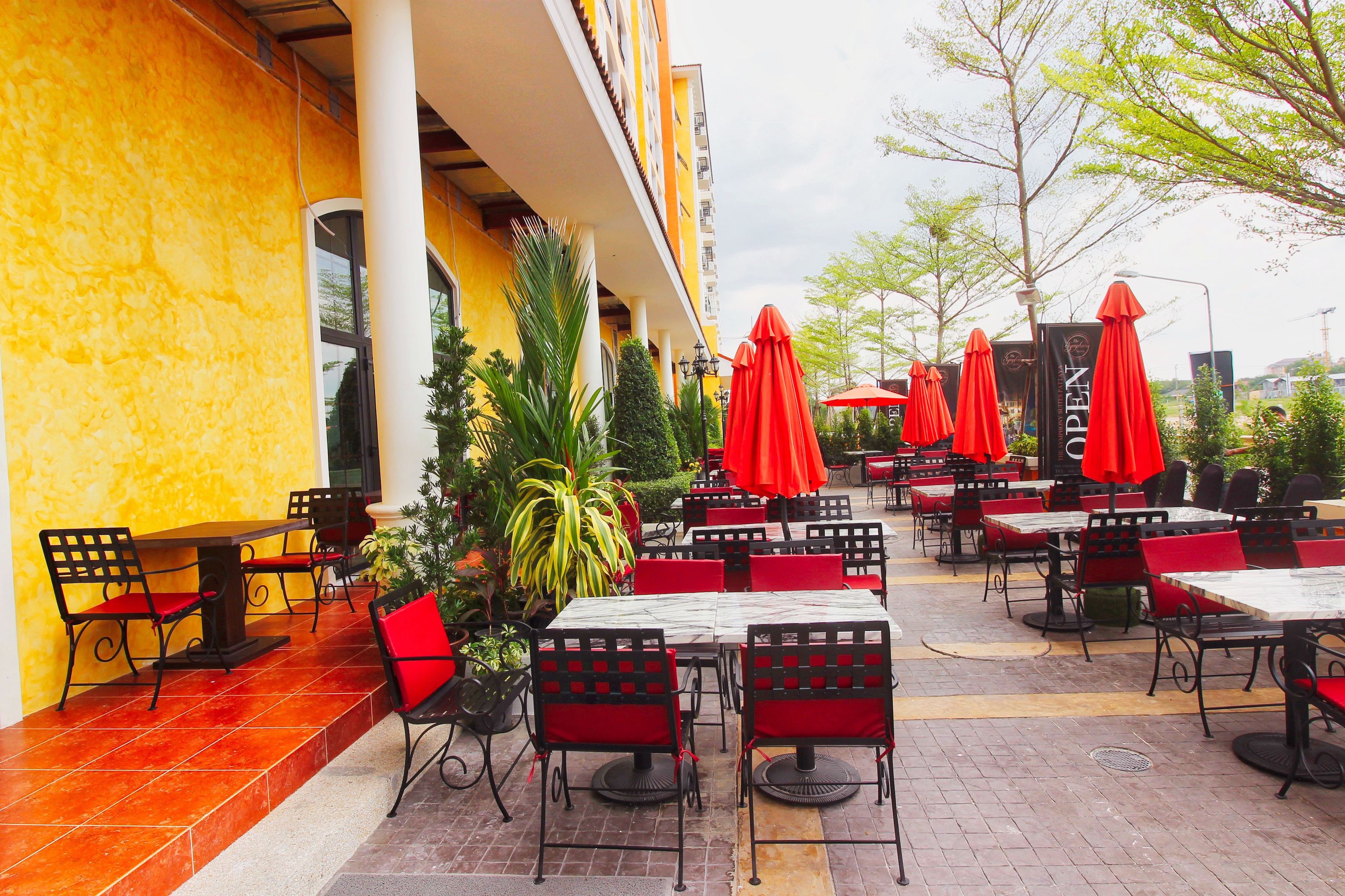 An outdoor cafe area with tables and chairs, red umbrellas, and a yellow building facade.