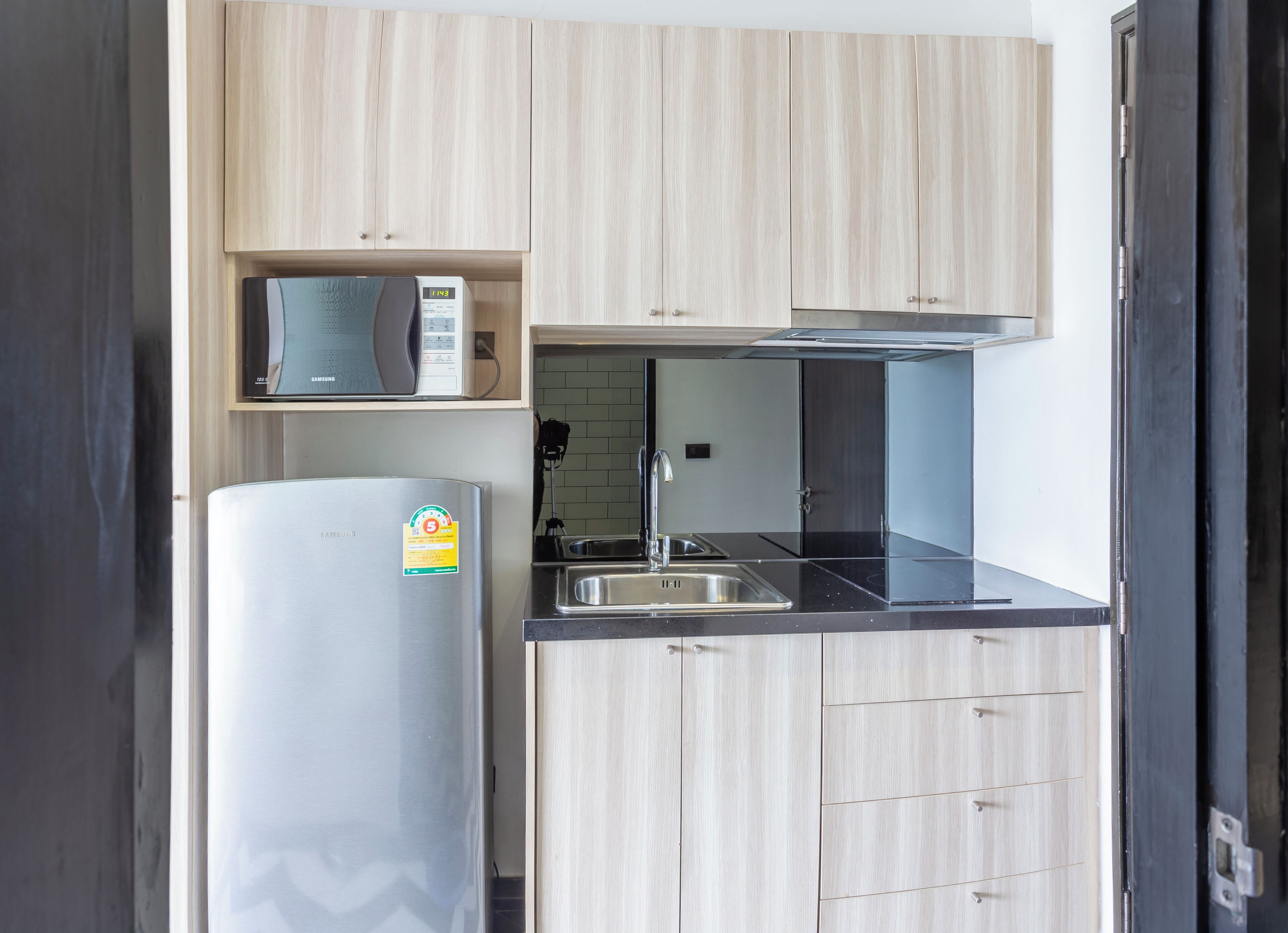 Een moderne keuken met lichte houten kastjes, een roestvrijstalen koelkast, een magnetron en een spoelbak.