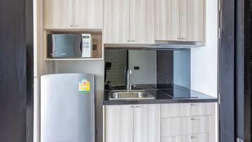 A modern kitchen with light wood cabinets, a stainless steel refrigerator, a microwave, and a sink.
