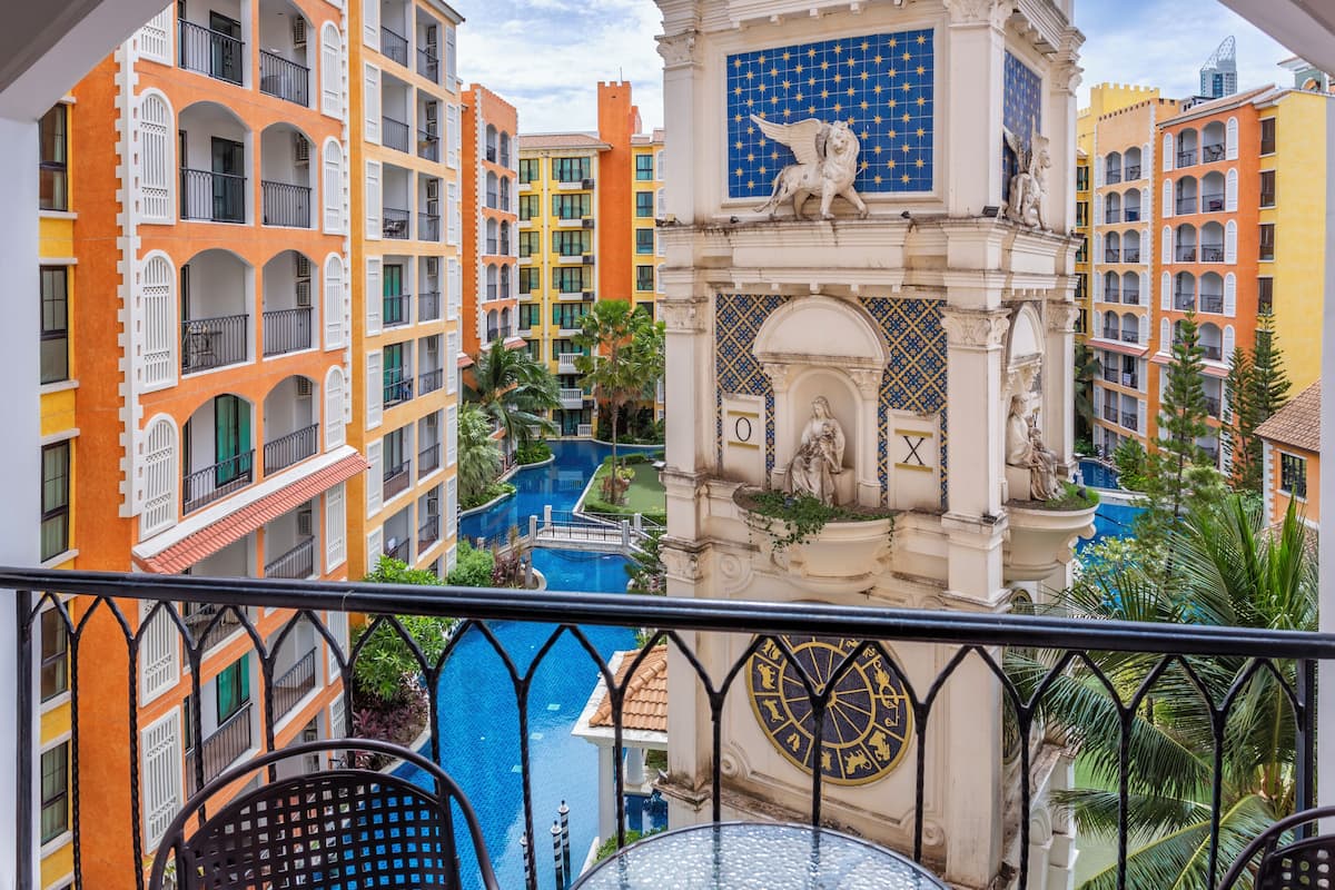 Vista de un hotel con varios balcones, un patio central con piscina y detalles arquitectónicos ornamentales, incluyendo estatuas y un reloj.