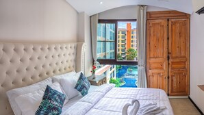 A hotel room with a large bed, a view of a swimming pool, and a wooden wardrobe.
