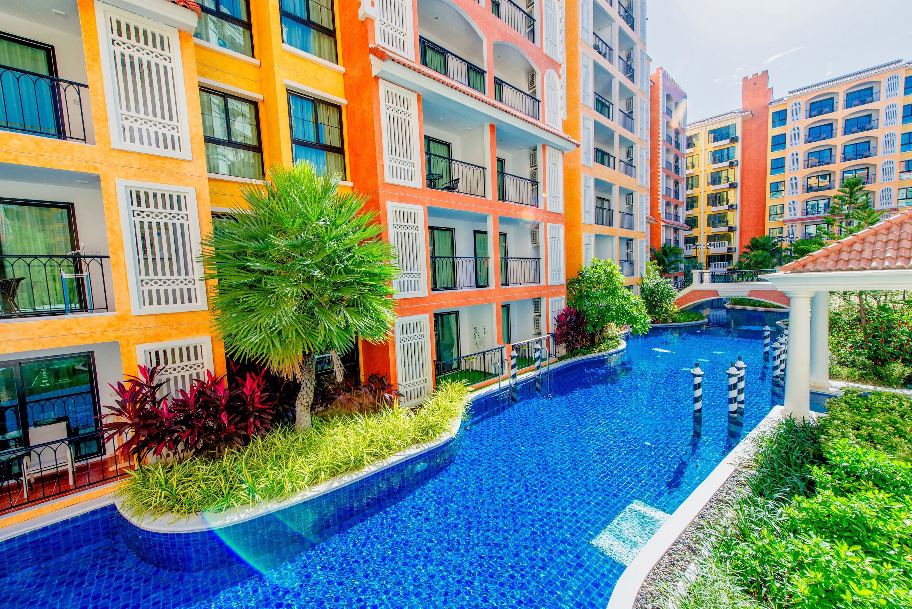 A multi-story hotel with balconies, a swimming pool, and lush landscaping.