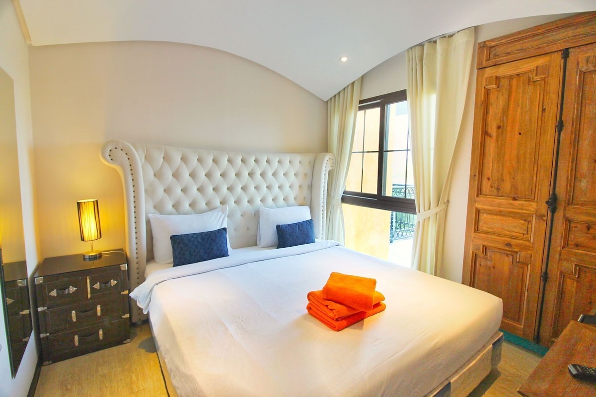 A hotel room with a large bed, a nightstand, a dresser, and a wooden wardrobe.