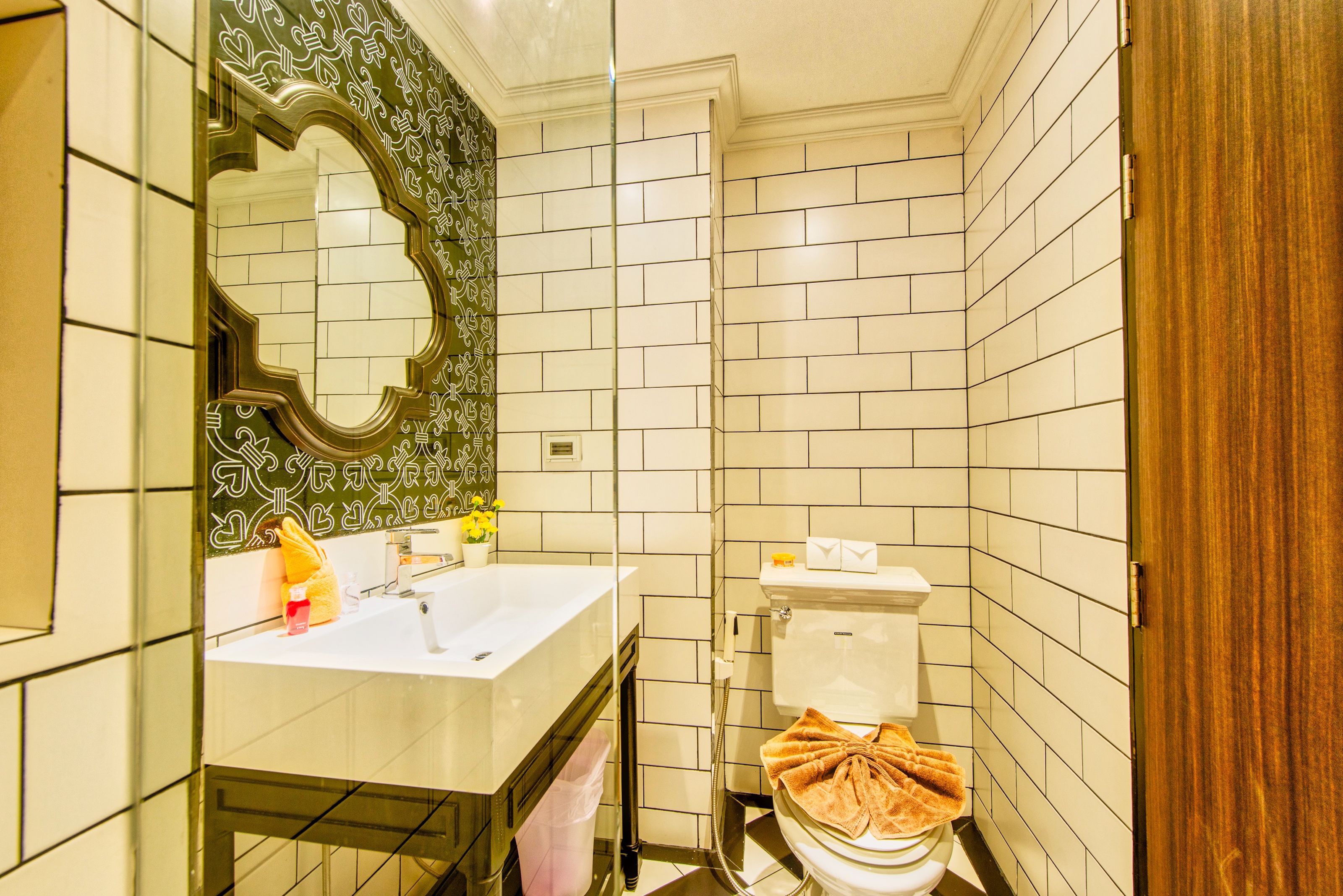 Un baño con un lavamanos blanco, un espejo con marco decorativo, un inodoro con una toalla y una puerta de madera.