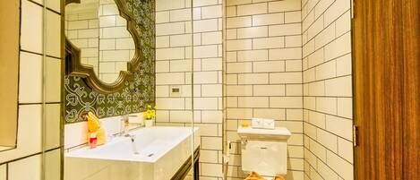 Un baño con un lavamanos blanco, un espejo con marco decorativo, un inodoro con una toalla y una puerta de madera.