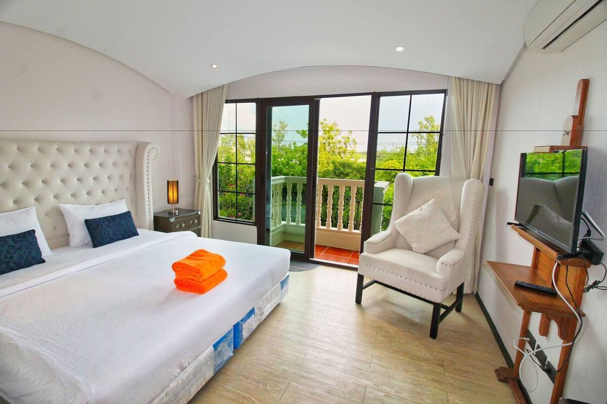 Habitación de hotel con cama, televisión, una silla y balcón con vistas.