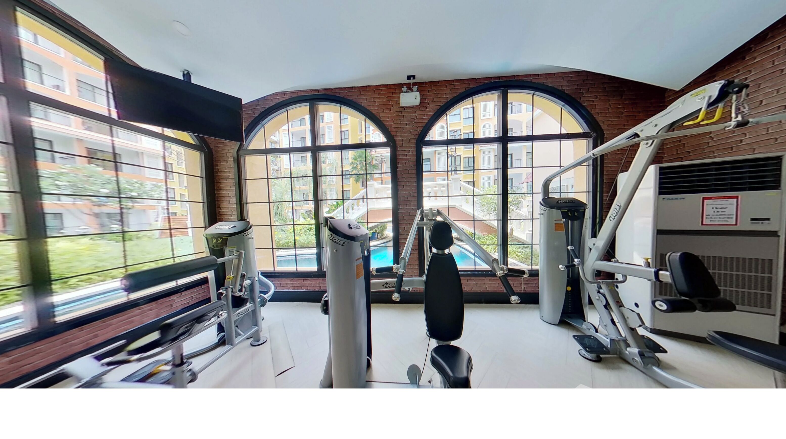 A gym with exercise equipment, large windows, and a brick wall.
