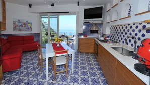 A modern kitchen with a large TV, a dining area with a red sofa, and a balcony with a city view. - Maison Lauren (Sorrento)