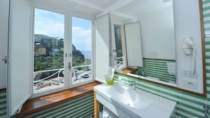 A bathroom with a large mirror, a sink, and a window with a view of buildings and greenery. - Maison Lauren (Sorrento)