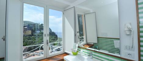 A bathroom with a large mirror, a sink, and a window with a view of buildings and greenery.