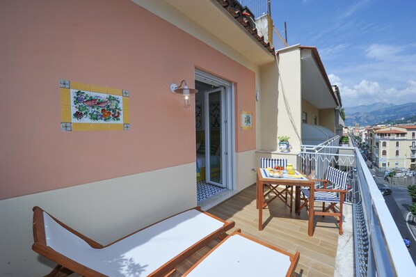 A balcony with two sun loungers, a table with chairs, and a decorative tile on the wall. - Maison Lauren (Sorrento)