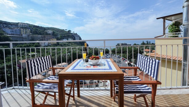 A balcony with a table set for two, a bowl of fruit, and two glasses of orange juice. - Maison Lauren (Sorrento)