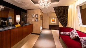 A hotel reception area with a reception desk, a chandelier, a red sofa, and a hallway leading to another room. - Phoenix Hotel (Hakuba)