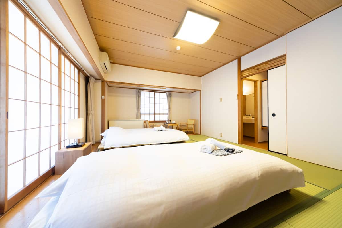 Habitación de hotel con dos camas, techo de madera, ventana con vistas, una mesita y una puerta.